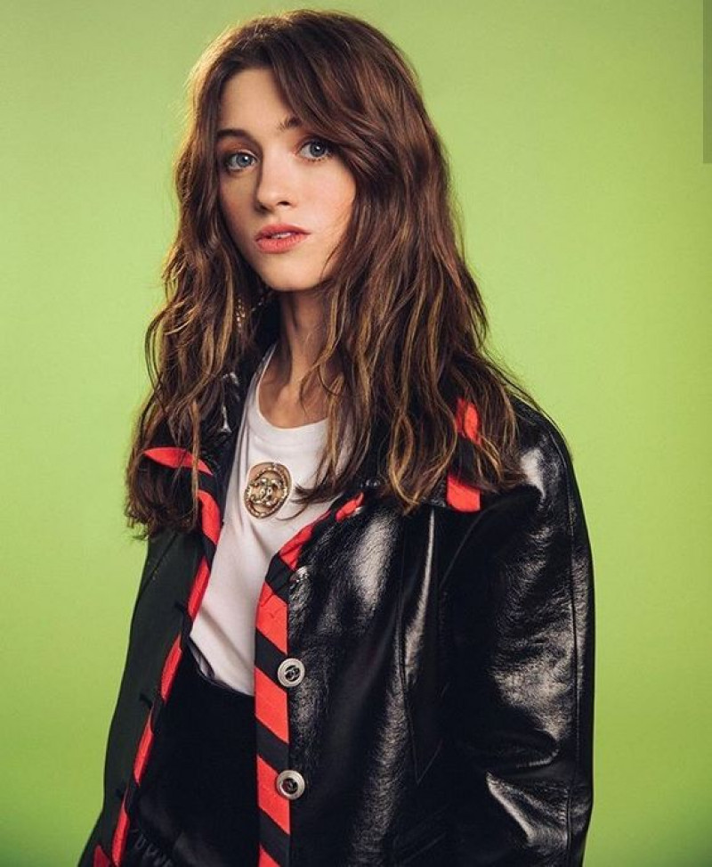 Natalia Dyer exudes confidence in a stunning black dress paired with bold red heels, showcasing glamorous elegance.: 
